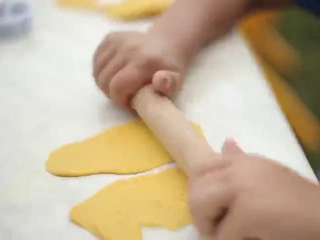 A child's hands rolling out dough with a rolling pin in the school garden